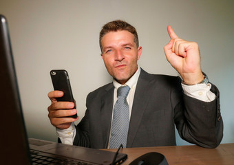 young happy and attractive businessman working with mobile phone at office computer desk celebrating success gesturing excited in corporate company job success