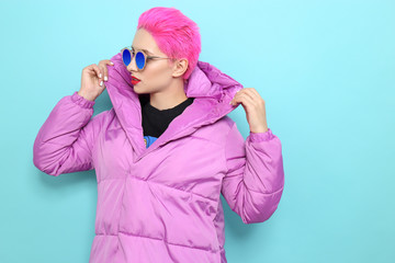 Wall Mural - Fashion portrait of young hipster woman in lilac down jacket. Short pink hair, sunglasses, red lips, turquoise background