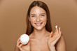 © Drobot Dean - Beauty image of european shirtless woman smiling and holding jar with face cream, isolated over beige background