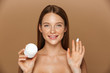 © Drobot Dean - Beauty image of young shirtless woman smiling and holding jar with face cream, isolated over beige background
