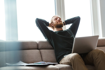 Young bearded man sitting in home using laptop computer.