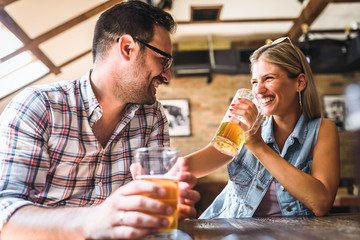 Wall Mural - Young cheerful couple in the beer pub drinking and having good time