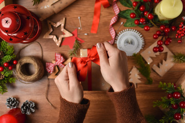 Woman decorating a handmade Christmas present on crafting table surrounded with all kind craft materials and decorations, top view