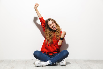 Sticker - Full length photo of joyous woman 20s wearing casual clothes smiling while sitting on floor with legs crossed, isolated over white background