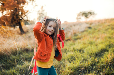 A small girl playing with a rainbow hand kite in autumn nature at sunset.