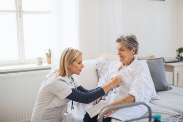 A health visitor helping a sick senior woman sitting on bed at home.