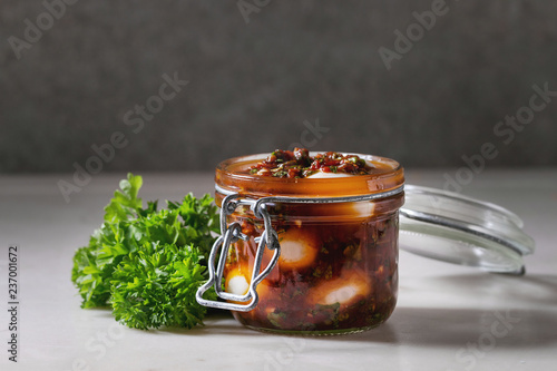 Fotografía Opened Jar with homemade pickled marinated quail eggs in tomato and olive oil sauce with anchovies and fresh parsley on white marble kitchen table