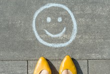 Symbol Of Happy Smiley Drawn On The Asphalt And Woman Feet