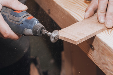 Wall Mural - hands of a man holding a Dremel tool with an installed small circular saw. Wood processing. Workshop. Manufacture of wooden products. Joiner's cutting tool