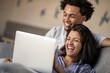 © FS-Stock - Cheerful happy African American young marriage laughing while watching movie on laptop computer at home interior.