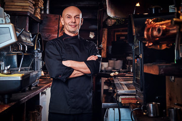 Confident chef posing with his arms crossed and looking at a camera in restaurant kitchen.