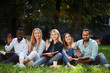 © alfa27 - group of young students sitting together on green lawn high school university campus