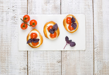 bruschetta with basil leaves and red cherry tomatoes on white basalt board on white wooden background