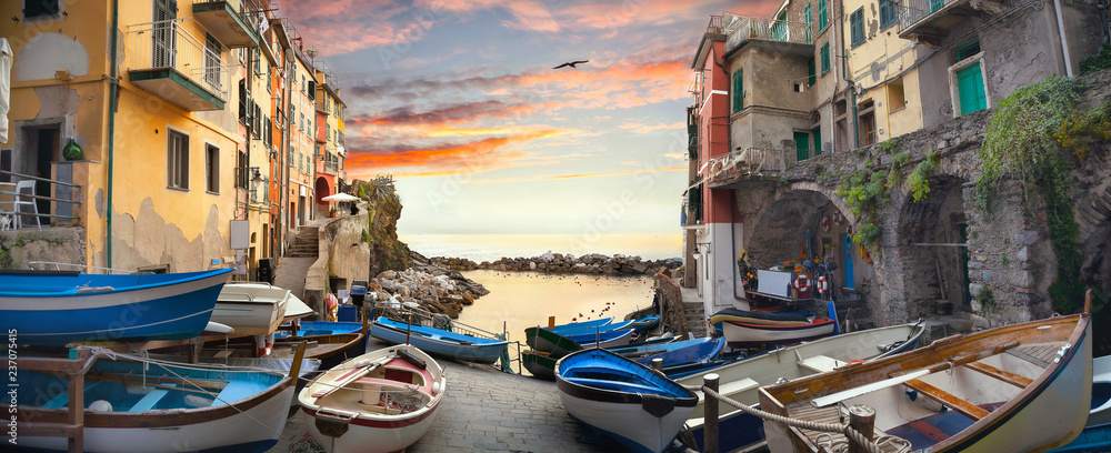Street with fishing boats and view of bay in village of Riomaggiore at sunset. Liguria, Italy - obrazy, fototapety, plakaty 