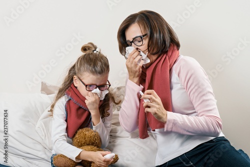 Fotografia Sick mother and child sneezing in handkerchief, holding nasal spray, cold season