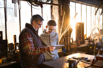 A craftsman and his young apprentice using a digital tablet