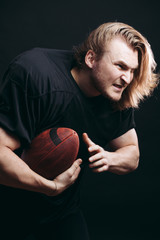 Wall Mural - American football team captain posing in motion with ball isolated on the black background, his face radiates aspiration for victory.