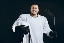 Happy Handsome Hockey Player With One Broken Front Tooth Laughing At Camera, Standing With Stick In White Uniform, Isolated On Black
