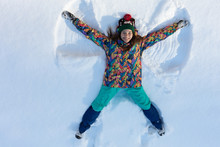 High Angle View Of Happy Girl Lying On Snow And Moving Her Arms And Legs Up And Down Creating A Snow Angel Figure. Smiling Woman Lying On Snow In Winter Holiday With Copy Space