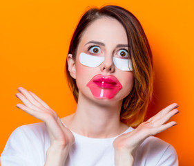 Woman using eye patch for her eyes and care lips on orange background isolated. Portrait of natural  and true female as usually they are looks like