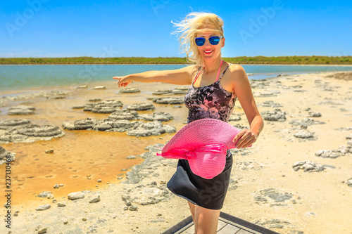 Happy woman pointing at Stromatolites on Lake Thetis, a saline coastal lake  in Cervantes, Western australia. Caucasian tourist enjoys of Australian  landscape in a sunny day with blue sky. - Buy this