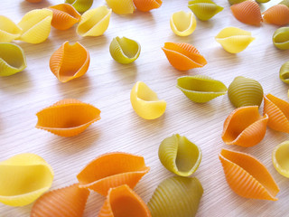 Textured Italian food background - colorful uncooked conchiglie pasta on wooden table