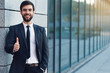 © speed300 - Portrait of smiling businessman showing thumb up  posing on background of office building