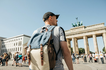 A tourist or a student with a backpack in Berlin in Germany visits the sights. Ahead is the Brandenburg Gate and unrecognizable blurred people.