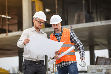 Male architect and developer discussing blueprints at construction site