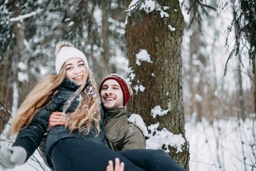  young couple in love are walking in the snowy winter forest. Positive beautiful lovers in clothes for the cold time.