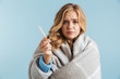 © Drobot Dean - Image of ill upset woman 20s wrapped in blanket holding thermometer, isolated over blue background