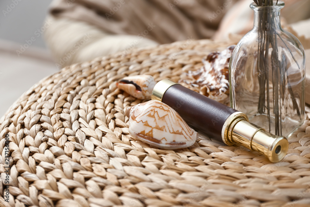Sea shells with spyglass on wicker table in interior of room
