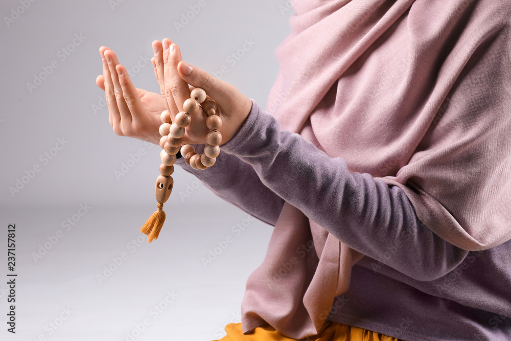 Muslim woman with beads praying on grey background