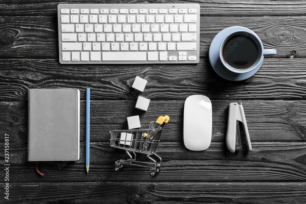 Composition with small cart, computer keyboard and cup of coffee on wooden background. Online shopping