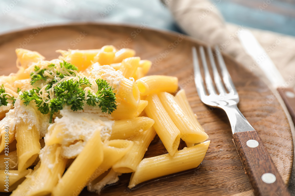 Tasty penne pasta on wooden plate, closeup
