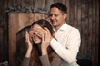 © Victoria Andreas - Happy Man covering woman's eyes with his hands. Surprised girl in cozy winter interior. Romantic couple portrait.