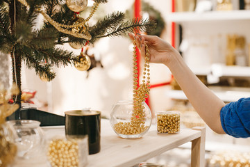 Pretty female hand grabbing gold beads for Christmas tree decoration, shopping woman hand with nude nails touching luxury gold Christmas decor displayed in shop