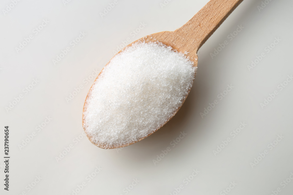 Granulated sugar in wooden spoon on white background