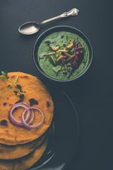 Makki di roti with sarson ka saag, popular punjabi main course recipe in winters made using corn breads mustard leaves curry. served over moody background. selective focus