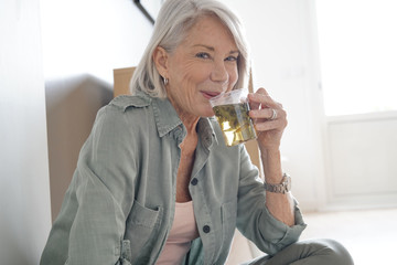 Wall Mural -  Attractive senior woman sitting on the floor at home with tea