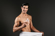 Handsome young man posing isolated over dark wall background holding toilet water covering genitals with towel.