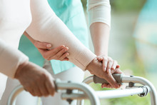 Closeup Of Senior Lady's Hands Holding A Walker And Helpful Nurse Supporting Her