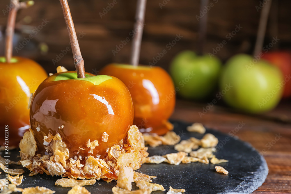 Delicious caramel apples with tree branches on slate plate