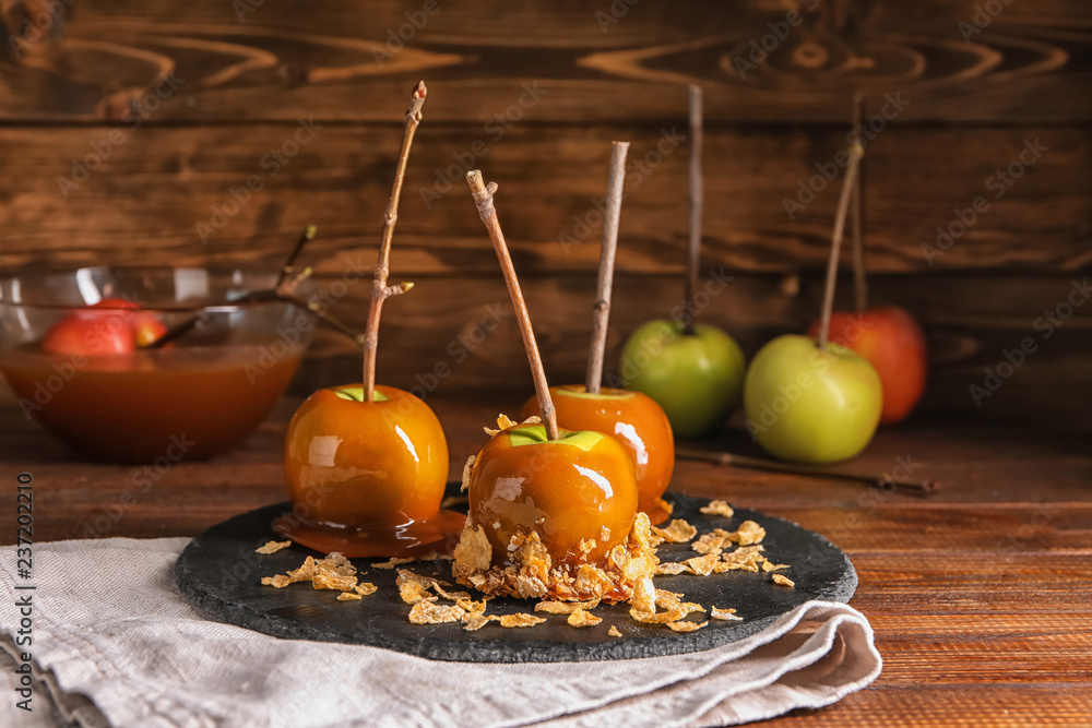 Delicious caramel apples with tree branches on slate plate
