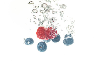 Wall Mural - Blueberry’s and raspberries splashing into crystal clear water with air bubbles and sinking white background