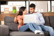 © Pixel-Shot - Young couple with laptop sitting on sofa at home