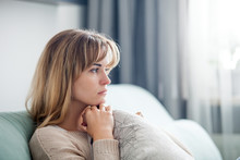 Depressed Woman Sitting On Sofa At Home, Thinking About Important Things