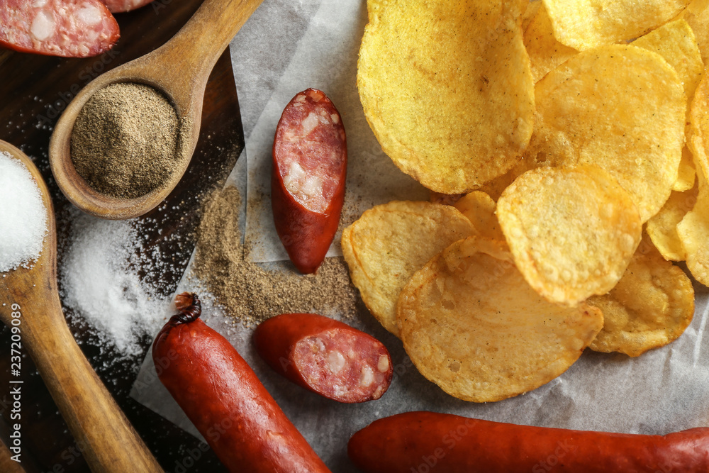 Tasty crispy potato chips with sausages on wooden board