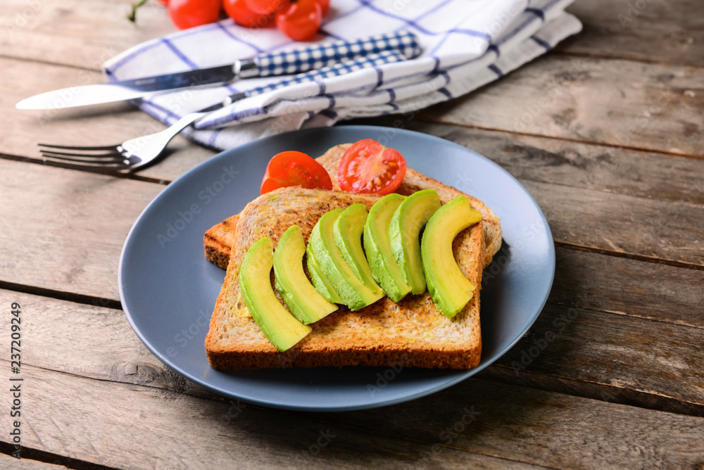 Plate with tasty toasted bread and avocado on wooden table