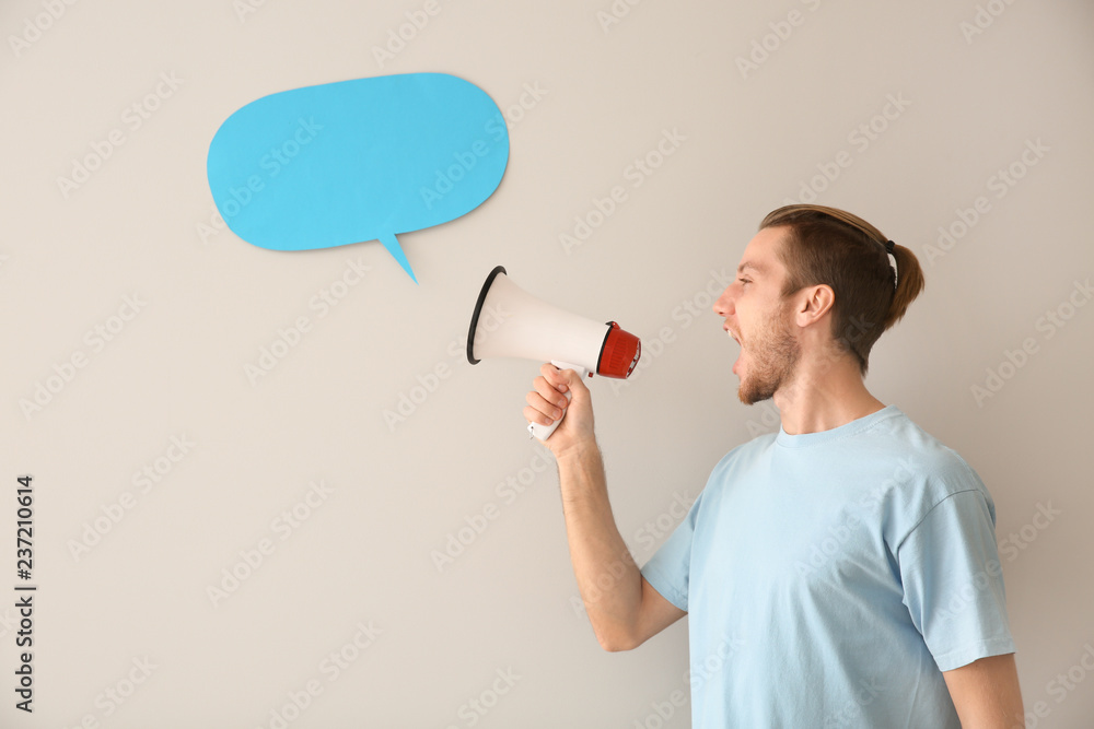 Screaming young man with megaphone and blank speech bubble on light background